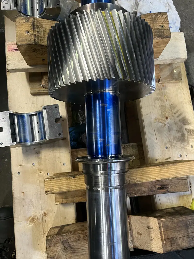 Helical gear shaft resting on blocks for inspection