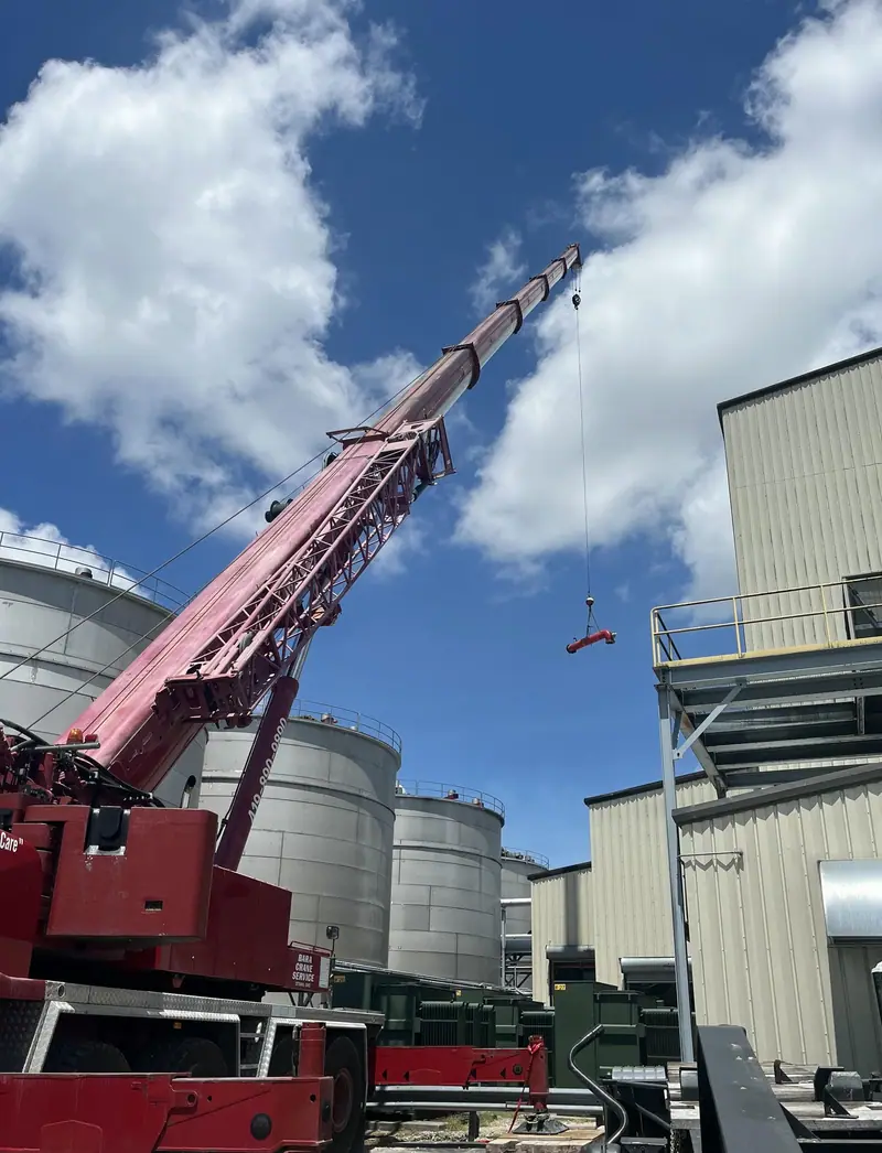 Mobile crane rigging a heavy lift beside plant silos